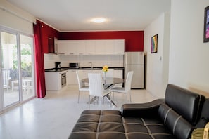 A modern kitchen with white cabinets, a dining table with chairs, and a black leather sofa.