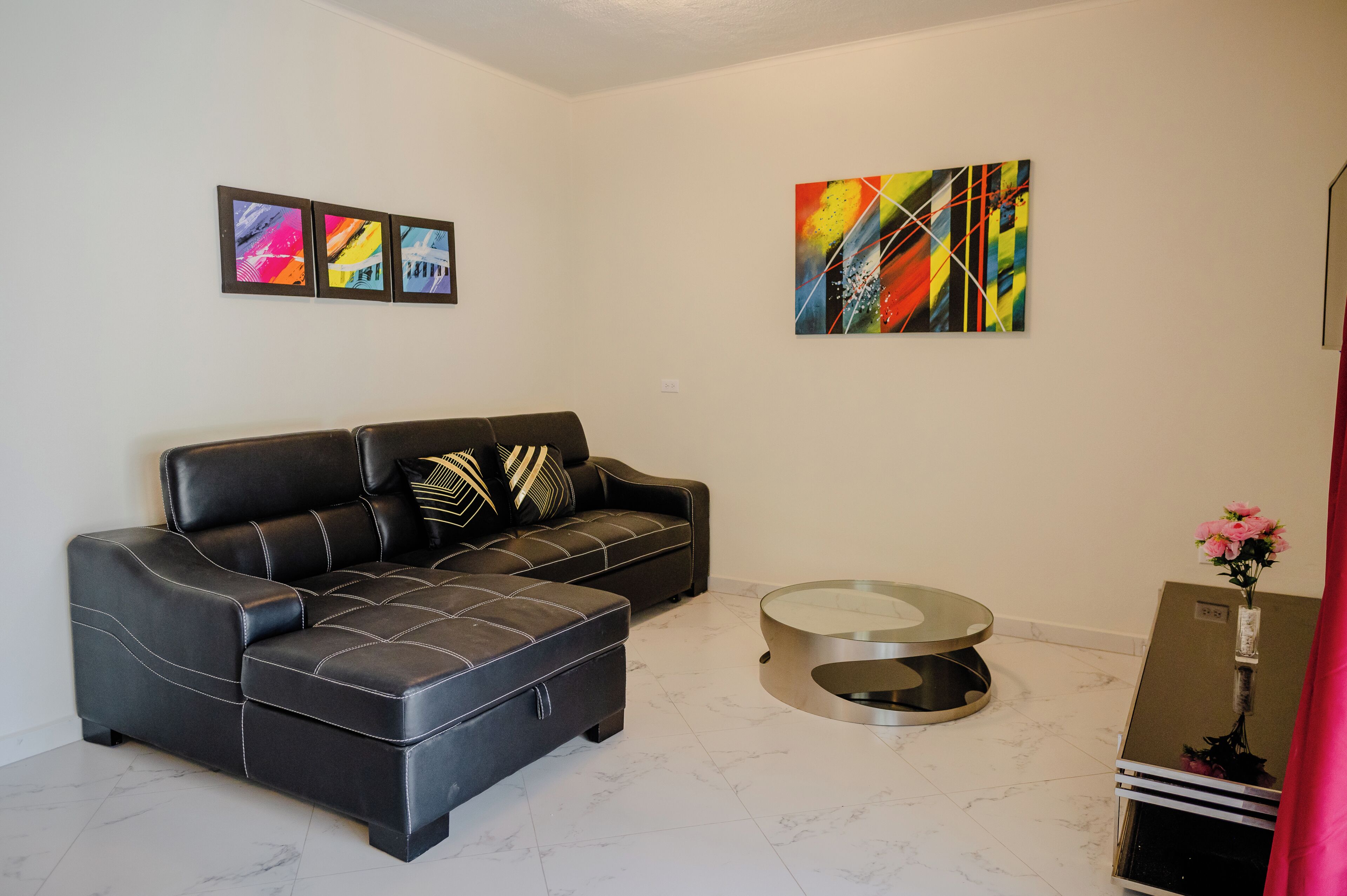 A modern living room with a black leather sofa, a glass coffee table, and abstract art on the walls.