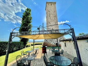 An outdoor patio with tables and chairs, a tall tower in the background, and a clear blue sky. - Luxurious Umbrian Villa With Private Pool and Stunning Views (Spello)