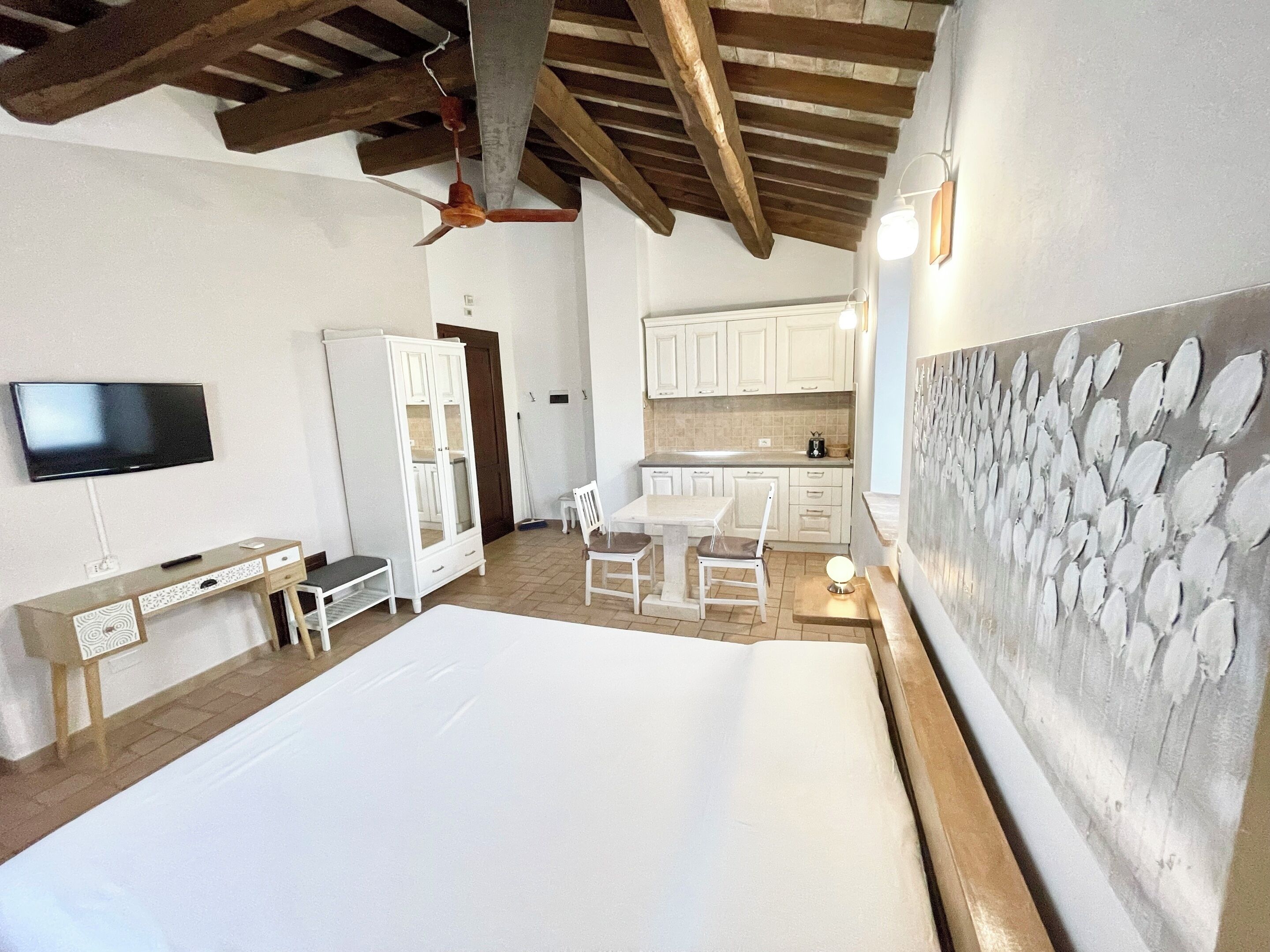Un dormitorio con una cama grande, un escritorio, una silla, un televisor, un armario y una zona de cocina con gabinetes.