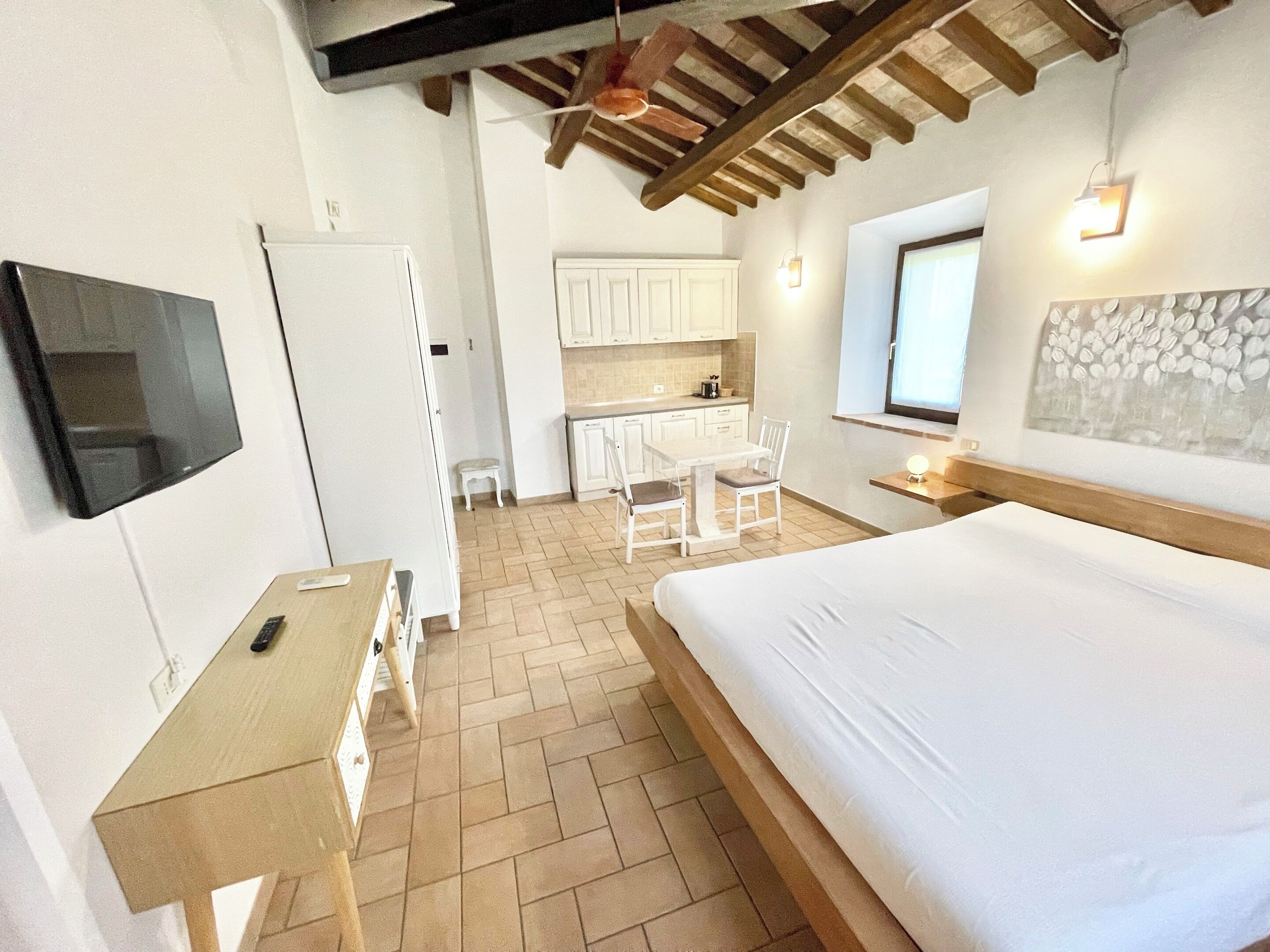 Una camera da letto con un letto, una scrivania, una sedia, una TV e un angolo cottura sullo sfondo.