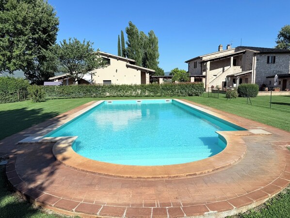 A rectangular swimming pool with a brick border, surrounded by a well-maintained lawn and a stone building in the background. - Luxurious Umbrian Villa With Private Pool and Stunning Views (Spello)