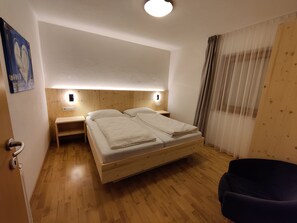 A hotel room with a wooden bed, bedside tables, a nightstand, a chair, and a painting on the wall. - Beautiful Residence Klementhof With Gard (Naz Sciaves)