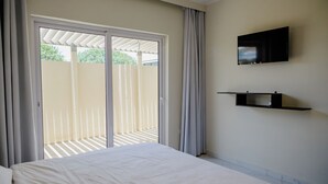 Une chambre à coucher avec un lit, un téléviseur fixé au mur et une porte-fenêtre coulissante donnant sur un balcon.
