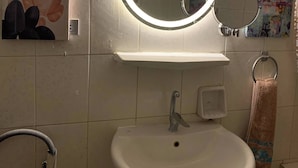 A bathroom with a white sink, a mirror with a light, and artwork on the walls. - Casa De Horyea , (Cairo)
