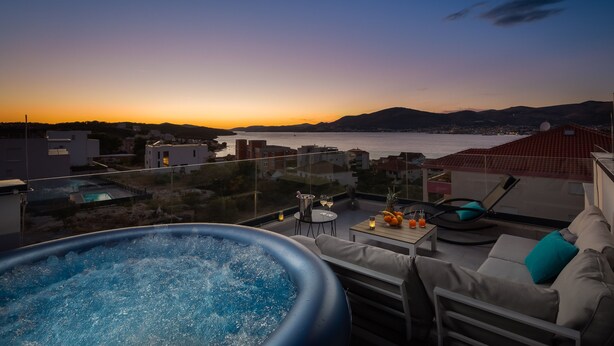Eine Dachterrasse mit Whirlpool, Sitzgelegenheit und Blick auf das Meer bei Sonnenuntergang.