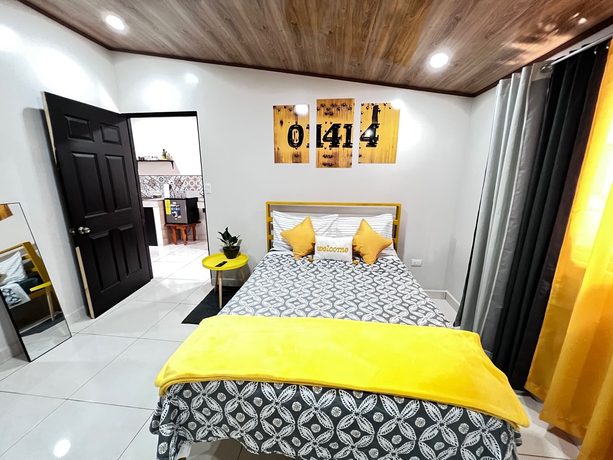 A bedroom with a bed, a yellow throw blanket, a wall clock, and a door leading to a bathroom.