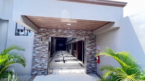 Una entrada moderna de edificio con fachada de piedra, un corredor cubierto y plantas en macetas.