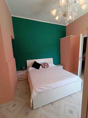 A bedroom with a white bed, teal walls, and a chandelier. - A Refuge Between Green And Blue (Tramonti)