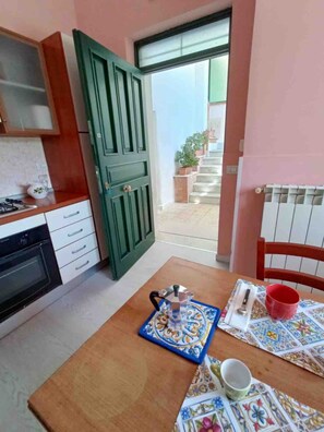 A kitchen with a stove, oven, and a table with a teapot, cup, and placemat. - A Refuge Between Green And Blue (Tramonti)