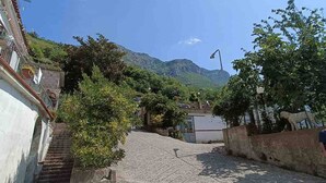 A narrow cobblestone street flanked by buildings, leading towards a mountain. - A Refuge Between Green And Blue (Tramonti)
