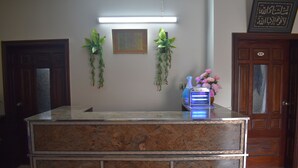 Una reception con un piano di lavoro in marmo, due piante in vaso, un quadro incorniciato e un distributore d'acqua blu.