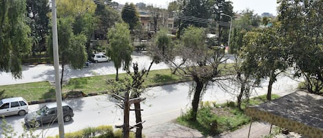 A residential street with parked cars, trees, and a building with a tiled roof.