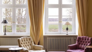 Ein Zimmer mit einem großen Fenster, einer Heizung, zwei Sesseln und einem kleinen Tisch.