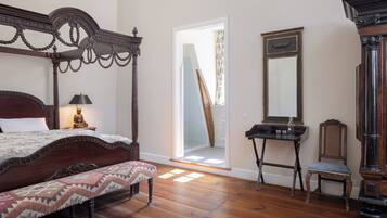 A bedroom with a wooden bed, a bench, a desk, a chair, and a large mirror.
