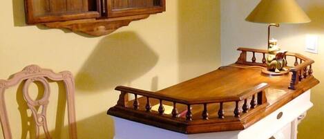 Un gabinete de madera con puerta de cristal, una silla blanca y una lámpara sobre una mesa de madera.