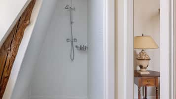 Un baño estrecho con pared de azulejos, una viga de madera y una pequeña mesa con lámpara.