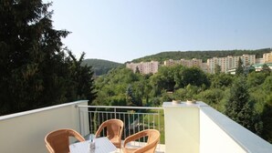 A balcony with wicker chairs and a table, overlooking a residential area with buildings and trees. - Penzion Vanessa (Brno)