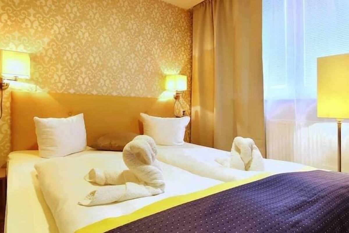 A hotel room with a large bed, two bedside lamps, and a nightstand with a lamp.