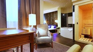 A hotel room with a wooden desk, a comfortable armchair, a bed with a patterned headboard, and a bathroom with a wooden door. - Penzion Vanessa (Brno)
