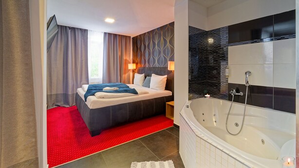 A modern bedroom with a large bed, a separate bathroom with a bathtub, and a red carpet. - Penzion Vanessa (Brno)