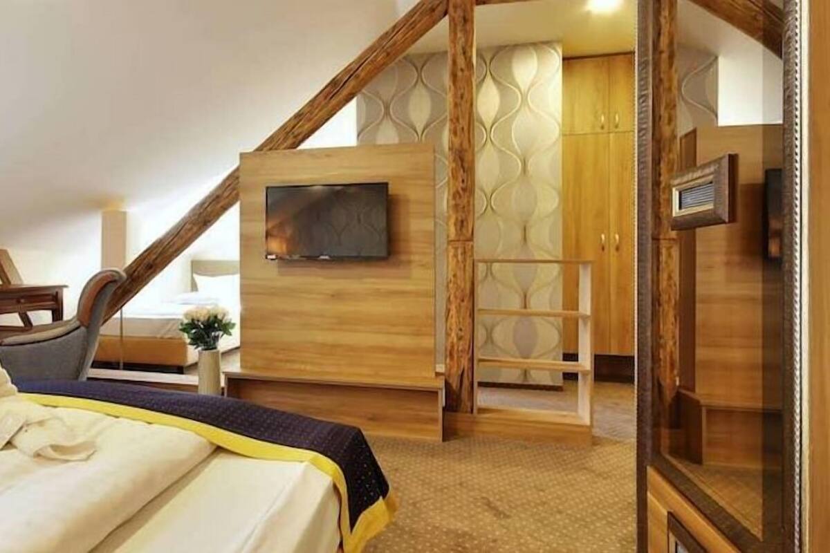 A bedroom with a bed, a desk, a chair, a TV mounted on the wall, and a wardrobe.