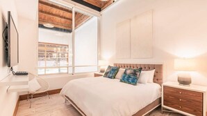A bedroom with a large bed, a desk, a chair, a TV, and a window with a view of a building. - Luxury Golf View Apartment near Casa de Campo (Casa De Campo)