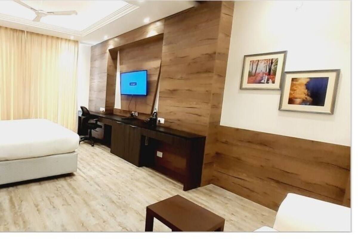 Ett hotellrum med en säng, ett skrivbord, en stol, en tv och konstverk på väggen.