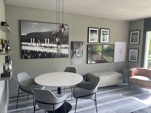 A modern living room with a round dining table, grey upholstered chairs, a beige sofa, and a large black-and-white photograph on the wall.