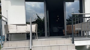 A modern building with a set of outdoor stairs leading to a glass door entrance, a white outdoor sofa, and a metal railing. - Garden Jewel Design Apartment (Minusio)