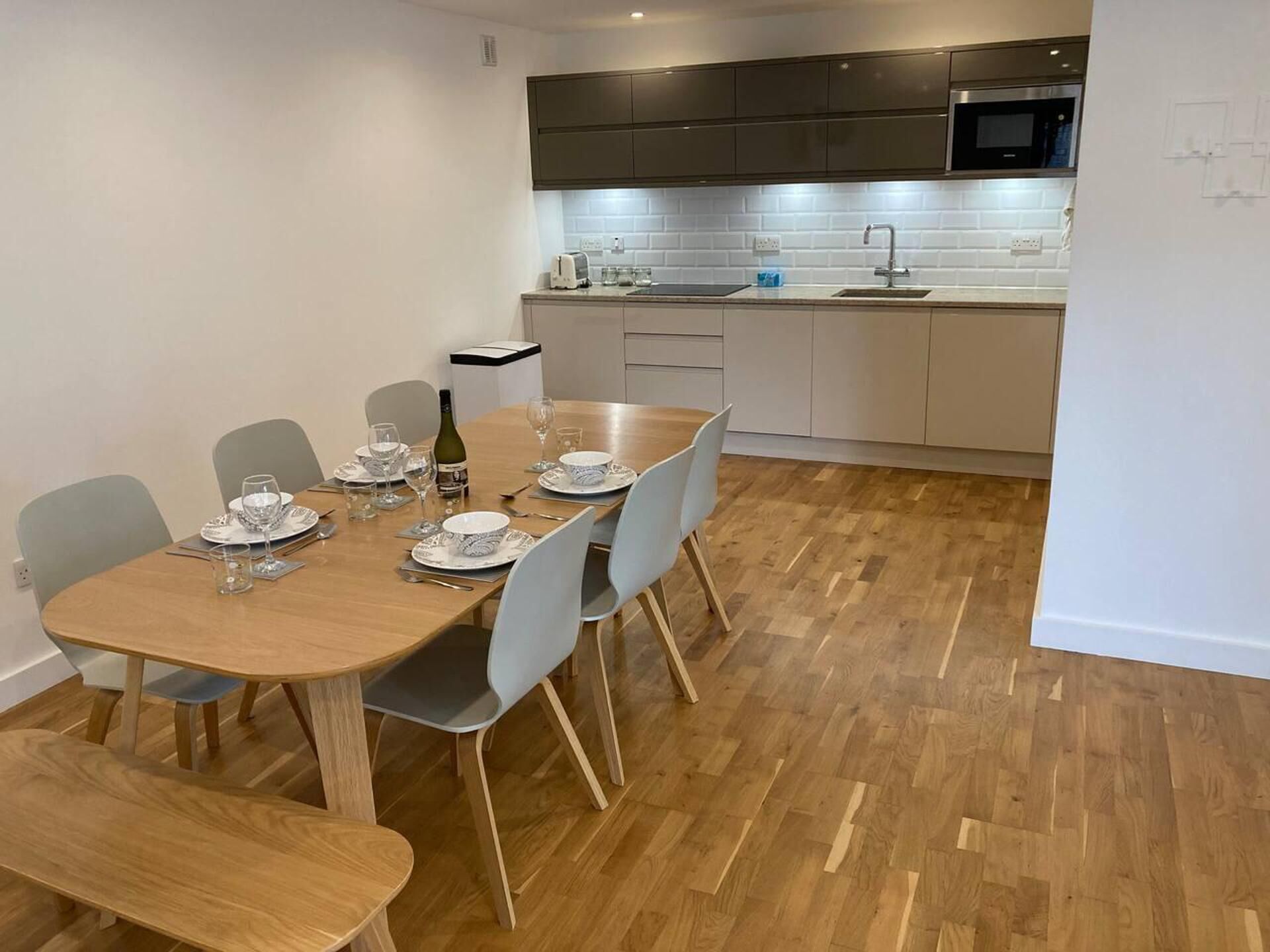 A modern kitchen with a wooden dining table set for four, a microwave, and a sink.