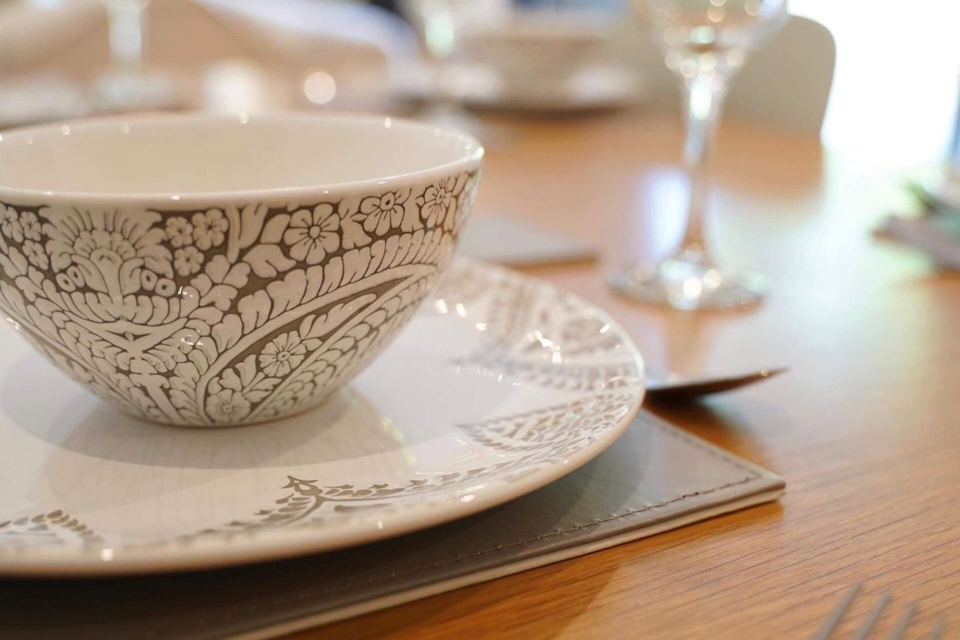 A white ceramic bowl with a floral pattern on a matching plate, placed on a wooden table.