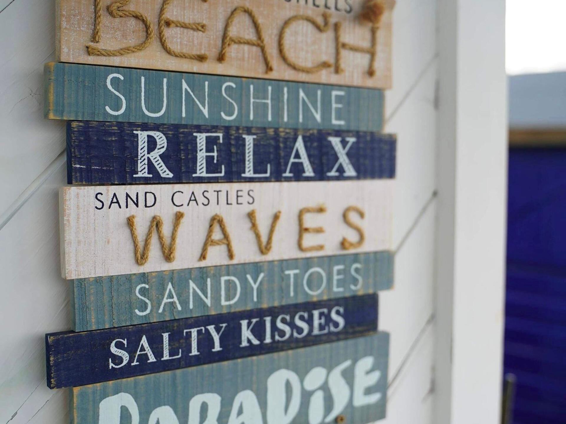 Uma parede com placas de madeira que exibem palavras como “PRAIA”, “SOL” e “RELAXAR”.