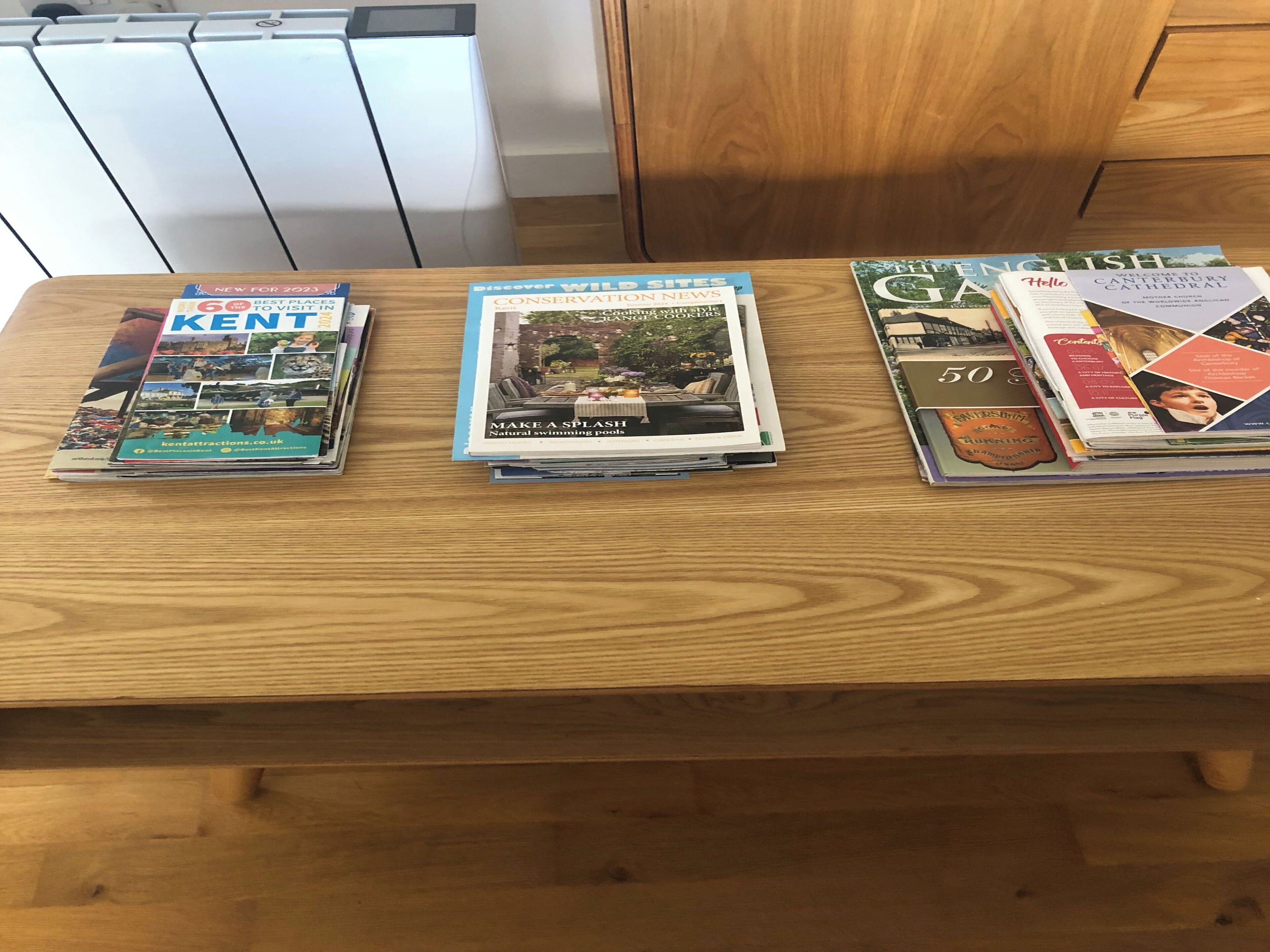Un tavolo di legno con tre riviste: 'Kent', 'Discover Wildlife News' e 'The English Garden'.