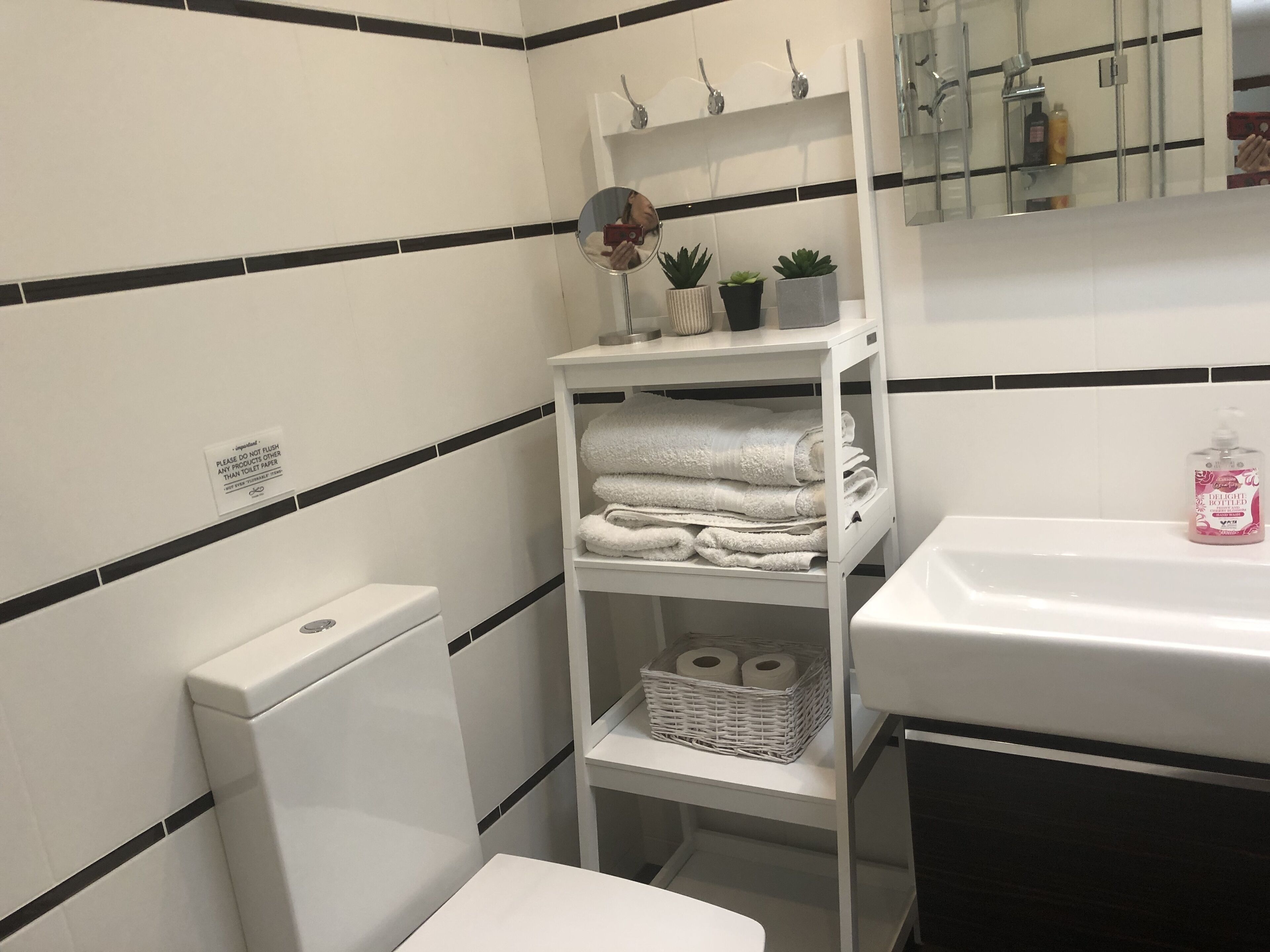 A bathroom with a toilet, a sink, a mirror, and shelves with towels and toiletries.