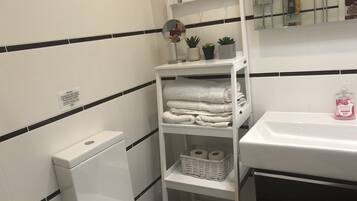 A bathroom with a toilet, a sink, a mirror, and shelves with towels and toiletries.