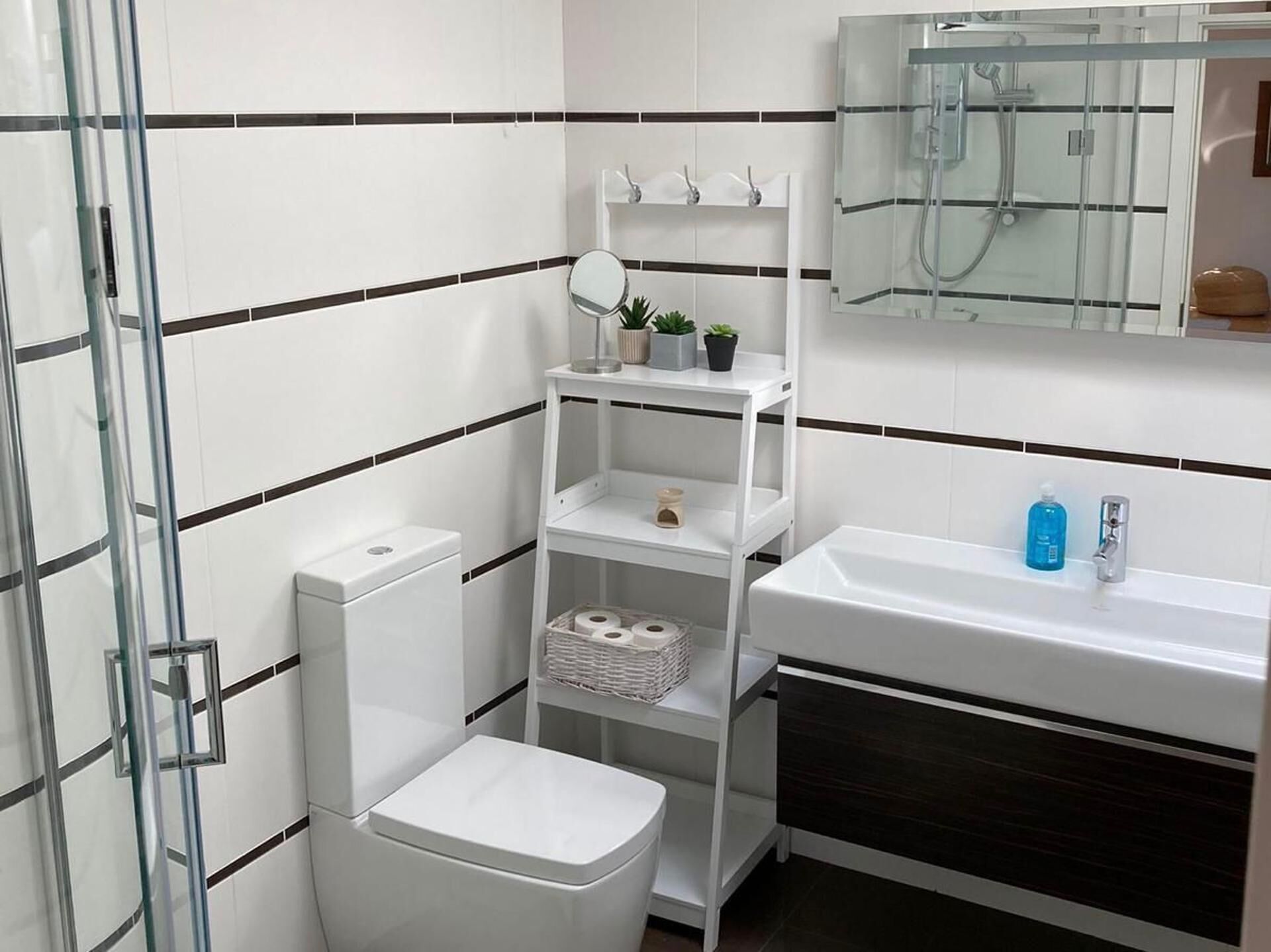 Un baño moderno con cabina de ducha de vidrio, inodoro blanco y tocador con espejo.