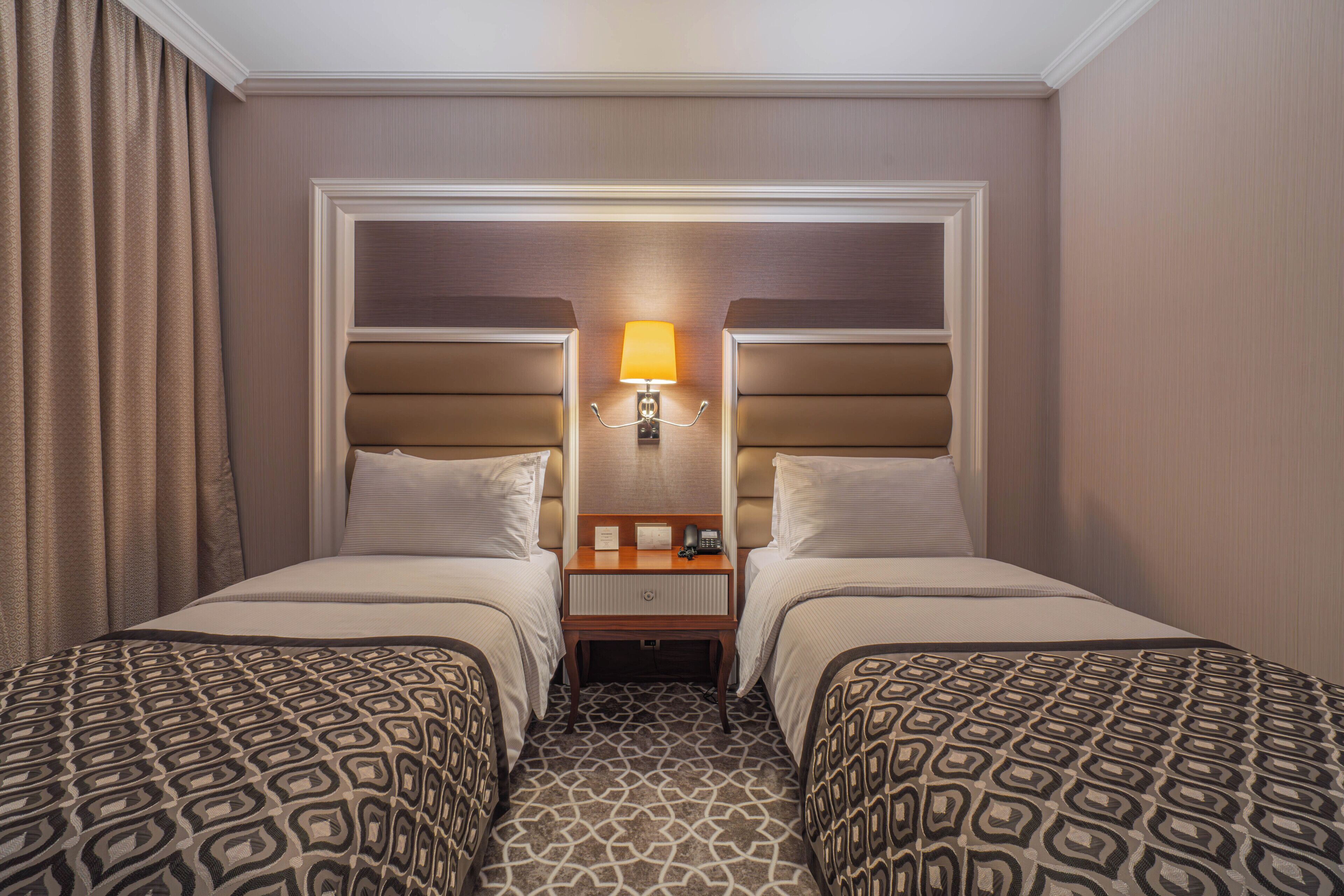 A hotel room with two beds, a nightstand with a lamp, and a patterned carpet.