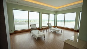 A spacious room with large windows, two lounge chairs, a small table, and a view of the sea. - Alusso Thermal Hotel & Spa (Afyonkarahisar)