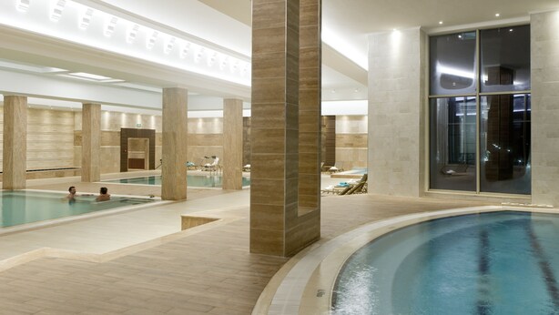 A large indoor swimming pool with multiple lanes, lounge areas with chairs, and a modern architectural design with large pillars and glass walls. - Alusso Thermal Hotel & Spa (Afyonkarahisar)