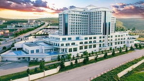 A modern hotel with a central tower and multiple wings, surrounded by greenery and a road. - Alusso Thermal Hotel & Spa (Afyonkarahisar)