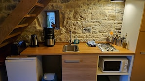 A compact kitchen with a stone wall, a wooden countertop, a built-in microwave, a sink, a coffee maker, a toaster, and a trash bin. - Small welcoming house in a farmhouse. (Parisot)