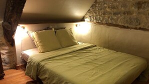 A bedroom with a bed, wooden floor, stone wall, and a sloped ceiling. - Small welcoming house in a farmhouse. (Parisot)
