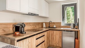 Moderni keittiö, jossa on puiset kaapit, ruostumattomasta teräksestä valmistettu astianpesukone, kahvinkeitin ja ikkuna, josta avautuu näkymä vehreään maisemaan.