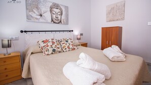 A neatly made bed with floral pillows, a wooden wardrobe, and artwork on the walls. - Alcazaba Square Central Beach (La Herradura)