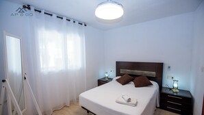 Une chambre à coucher bien rangée, avec un lit, deux tables de chevet, une commode, un luminaire au plafond et une fenêtre ornée de rideaux légers.
