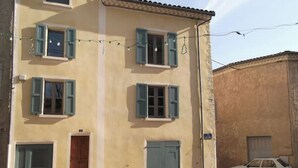 A two-story building with a beige facade, green shutters, and a wooden door. There is a parked white car in the foreground. - Charming village house (Buis-les-Baronnies)