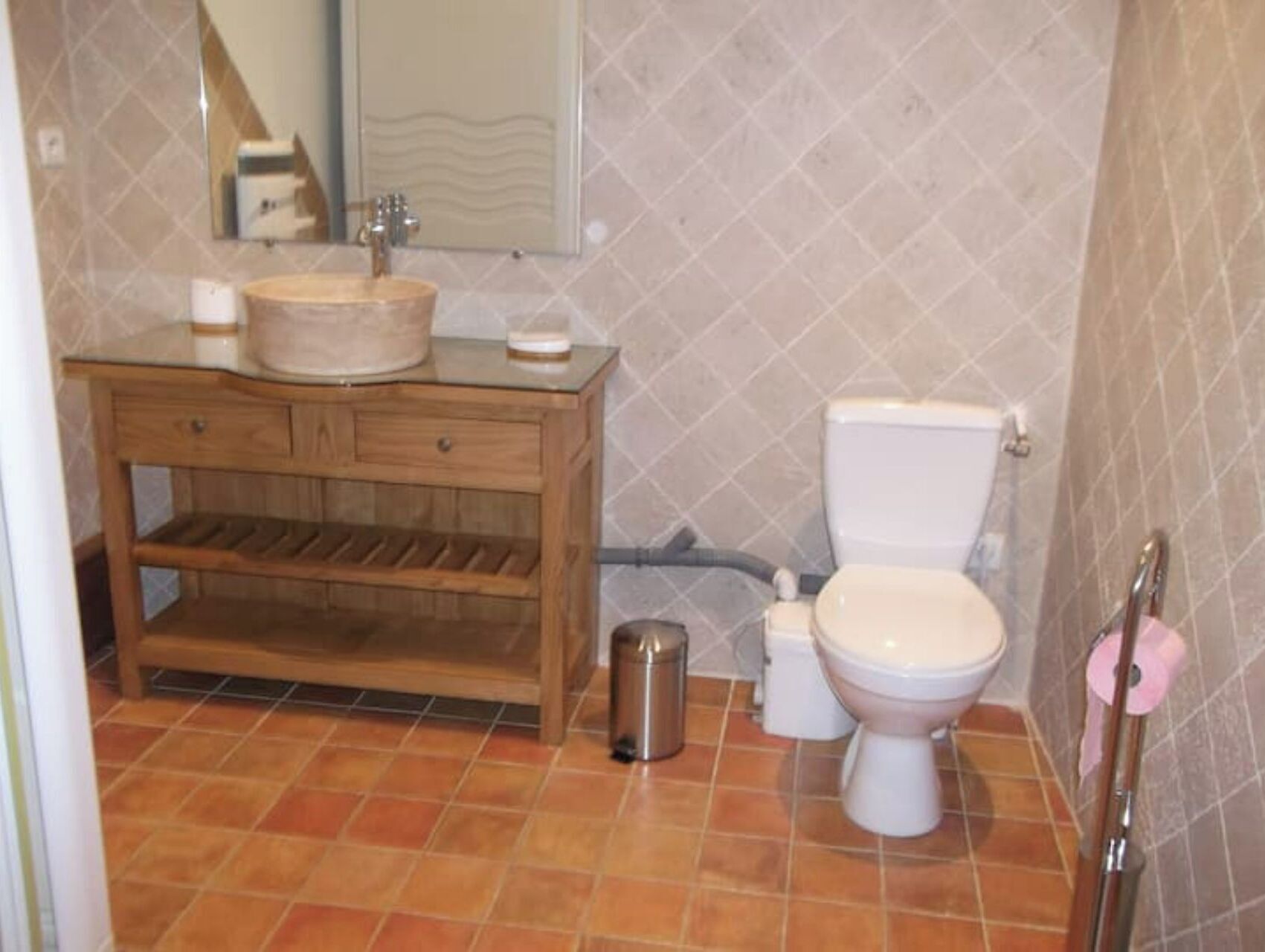 A bathroom with a wooden vanity, a sink, a toilet, and a trash can.