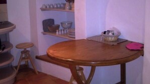 A kitchen with a round wooden table, a stool, and shelves with kitchenware. - Charming village house (Buis-les-Baronnies)