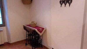 A small kitchen with a table and stools, a hanging basket, and a wall-mounted decoration. - Charming village house (Buis-les-Baronnies)